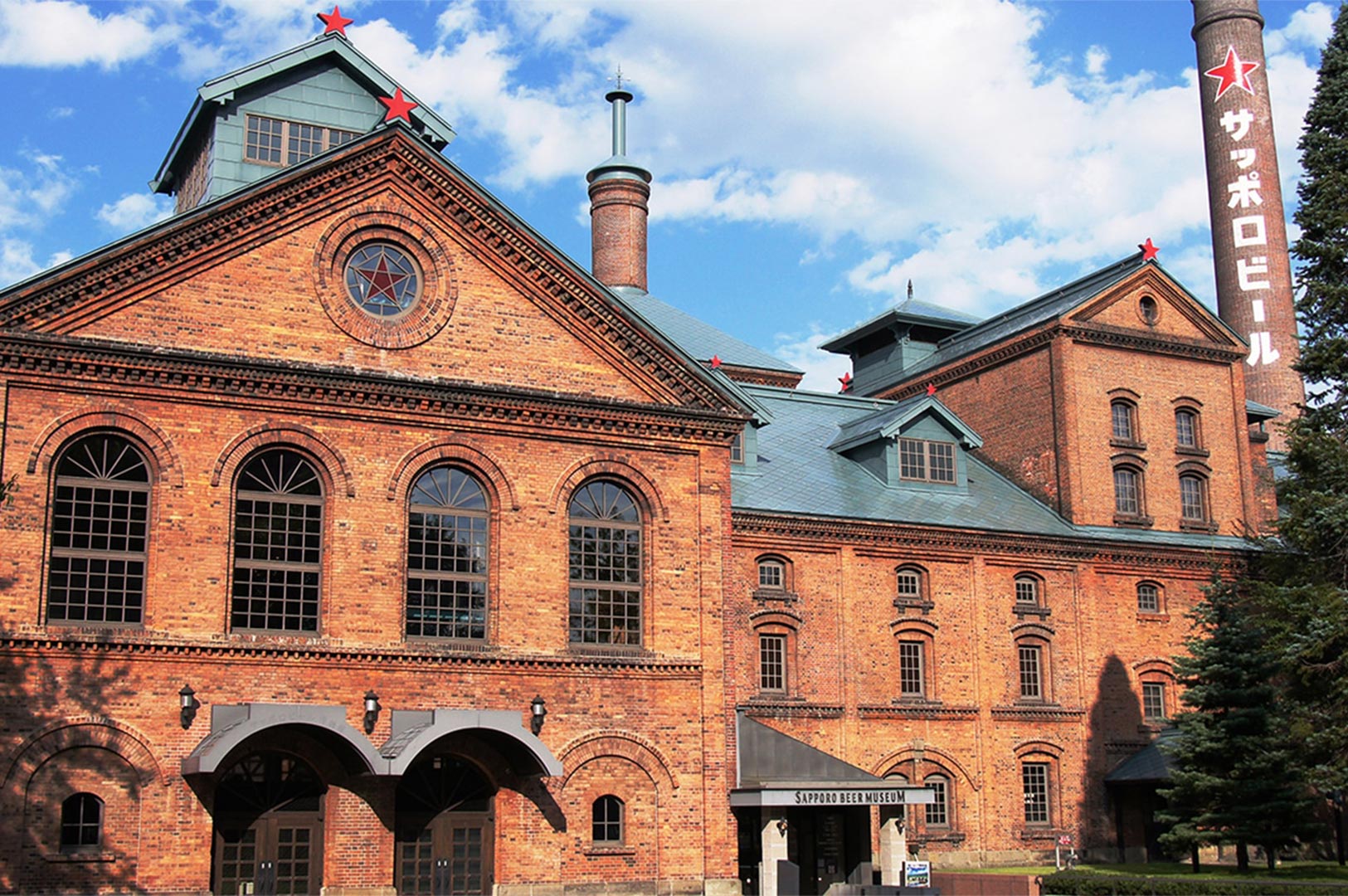 The historic red brick exterior of the Sapporo Beer Museum in Hokkaido, featuring its iconic chimney with a red star and blue sky background.