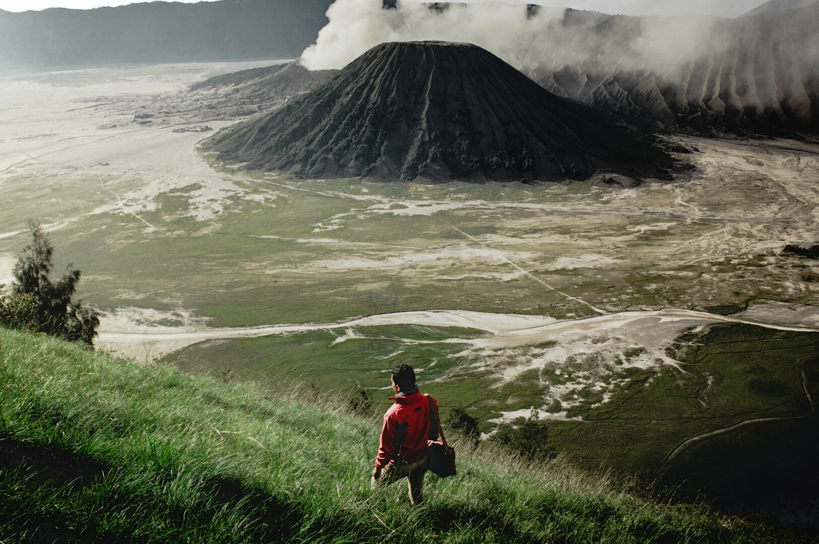 A man overlooks a volcano from a hill, reflecting the philosophy of taking time to appreciate travel experiences.