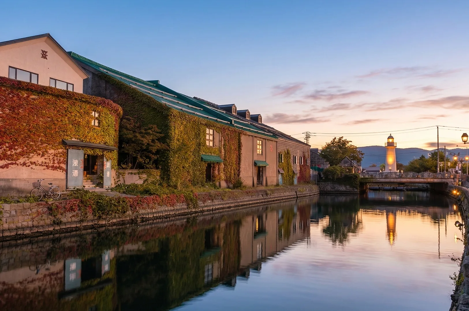 A serene sunset view of the Otaru Canal in Hokkaido, Japan, featuring ivy-covered stone warehouses reflected in the water and a glowing lighthouse in the distance.