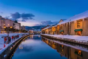 Scenic night view of the Otaru Canal in winter with snow-covered warehouses, glowing gas lamps, and reflections on the water.