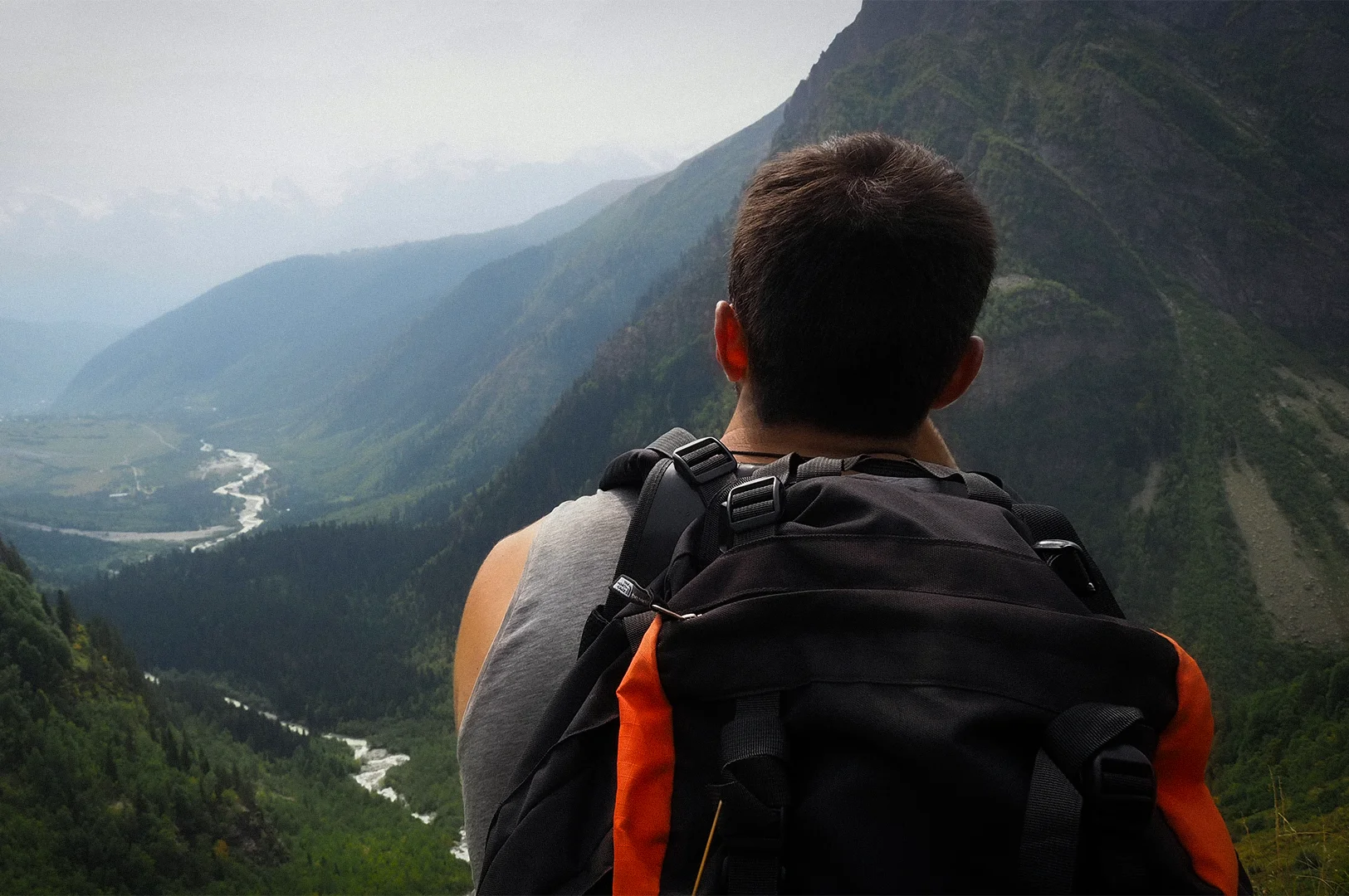 Backpacker overlooking a vast mountain valley with winding rivers and forested cliffs during a scenic hiking adventure in the mountains
