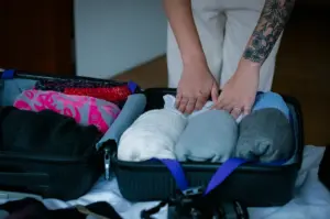 Woman packing clothes into a suitcase using pink striped travel organizers and packing cubes while preparing for a trip at home