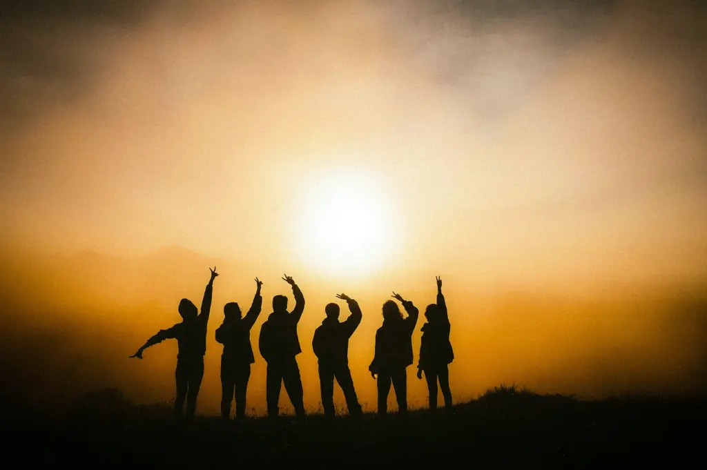 Silhouettes of friends celebrating at sunrise on a mountain ridge with golden sunlight, misty landscapes, and scenic outdoor adventure views.