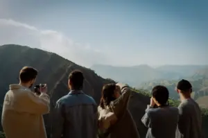 Group of travelers overlooking a scenic mountain landscape while sightseeing and taking photos during an outdoor adventure trip.