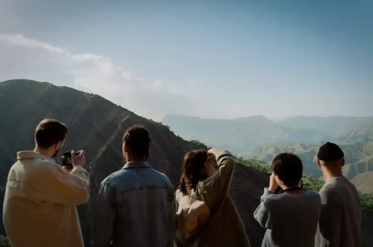 Group of travelers overlooking a scenic mountain landscape while sightseeing and taking photos during an outdoor adventure trip.