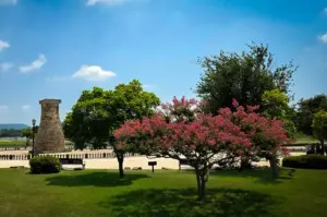 Scenic park in Gyeongju, South Korea featuring manicured gardens, flowering trees, open green lawns, and a historic stone structure under a clear blue sky.