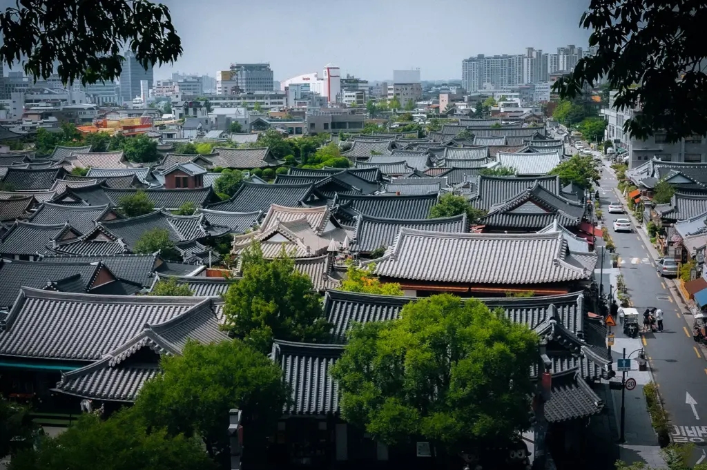 Panoramic view of Jeonju Hanok Village in South Korea featuring traditional Korean hanok rooftops, tree-lined streets and the modern city skyline in the background.