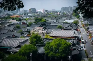 Panoramic view of Jeonju Hanok Village in South Korea featuring traditional Korean hanok rooftops, tree-lined streets and the modern city skyline in the background.