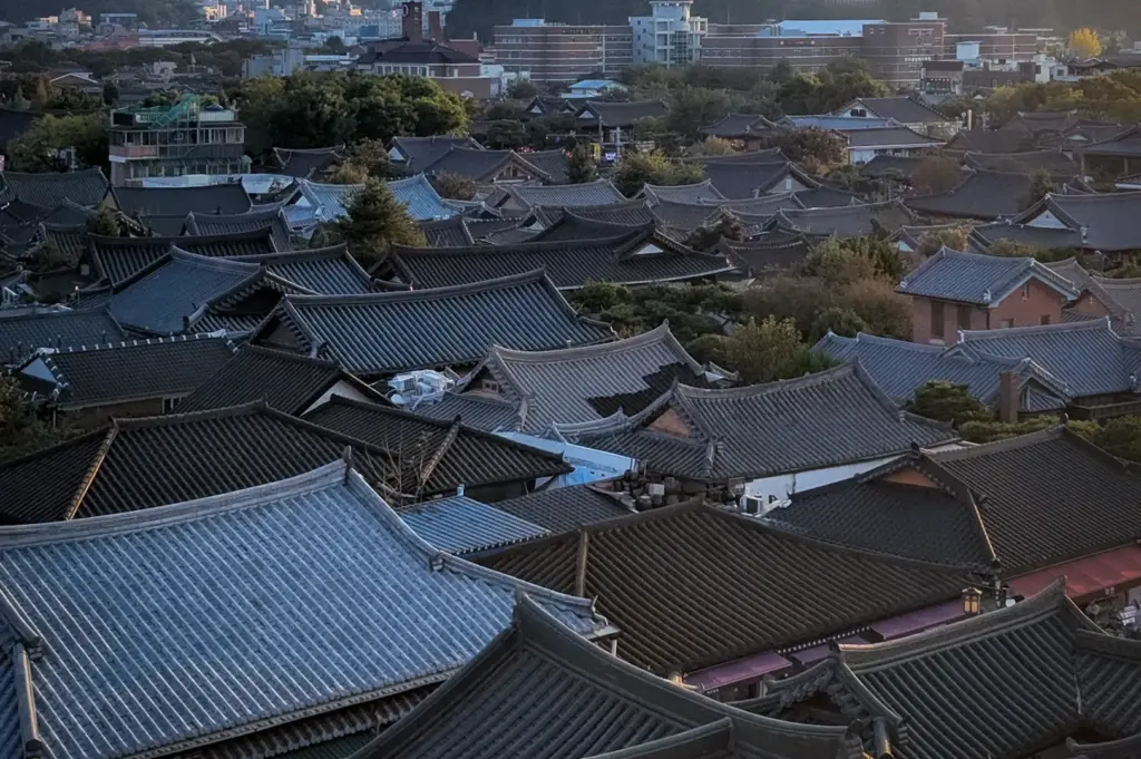 Panoramic view of Jeonju Hanok Village featuring traditional Korean hanok rooftops, historic architecture, and surrounding hills illuminated by warm evening light in Jeonju, South Korea.