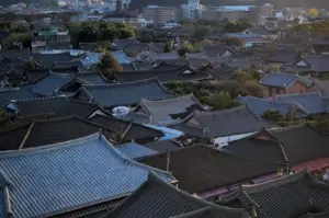 Panoramic view of Jeonju Hanok Village featuring traditional Korean hanok rooftops, historic architecture, and surrounding hills illuminated by warm evening light in Jeonju, South Korea.