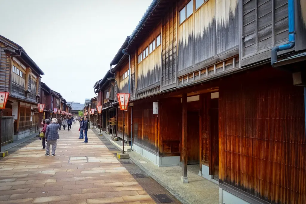 Traditional wooden machiya buildings line a stone-paved street in Kanazawa's Higashi Chaya District, Japan, with visitors strolling through the preserved historic geisha quarter adorned with lanterns.