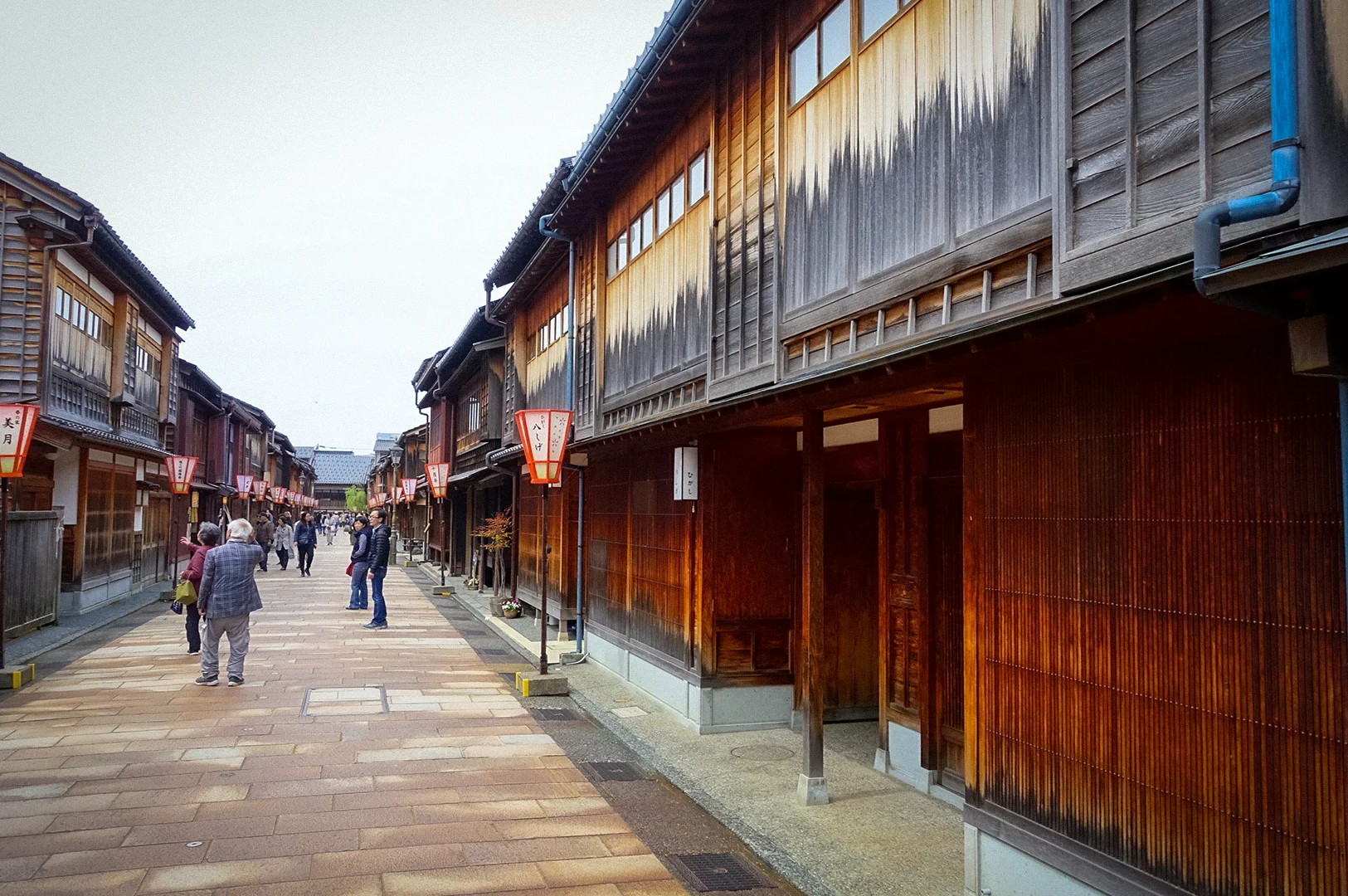 Traditional wooden machiya buildings line a stone-paved street in Kanazawa's Higashi Chaya District, Japan, with visitors strolling through the preserved historic geisha quarter adorned with lanterns.