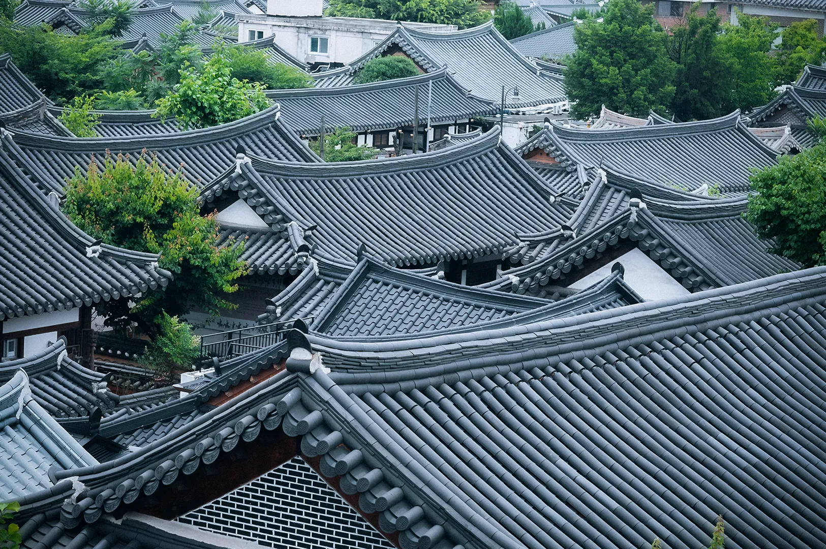 Scenic view of Jeonju Hanok Village in South Korea featuring traditional Korean hanok rooftops, lush greenery and surrounding hills in the background.