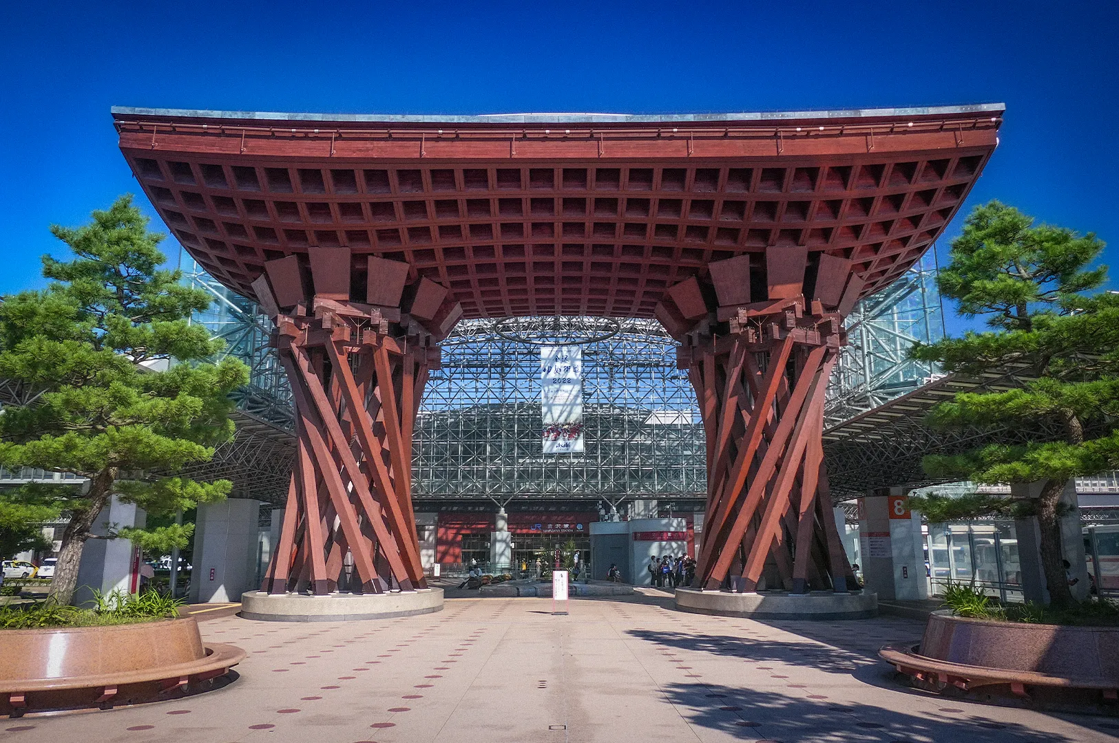 Tsuzumi-mon Gate at Kanazawa Station in Japan, showcasing traditional wooden-inspired architecture and the modern glass station facade under a clear blue sky.