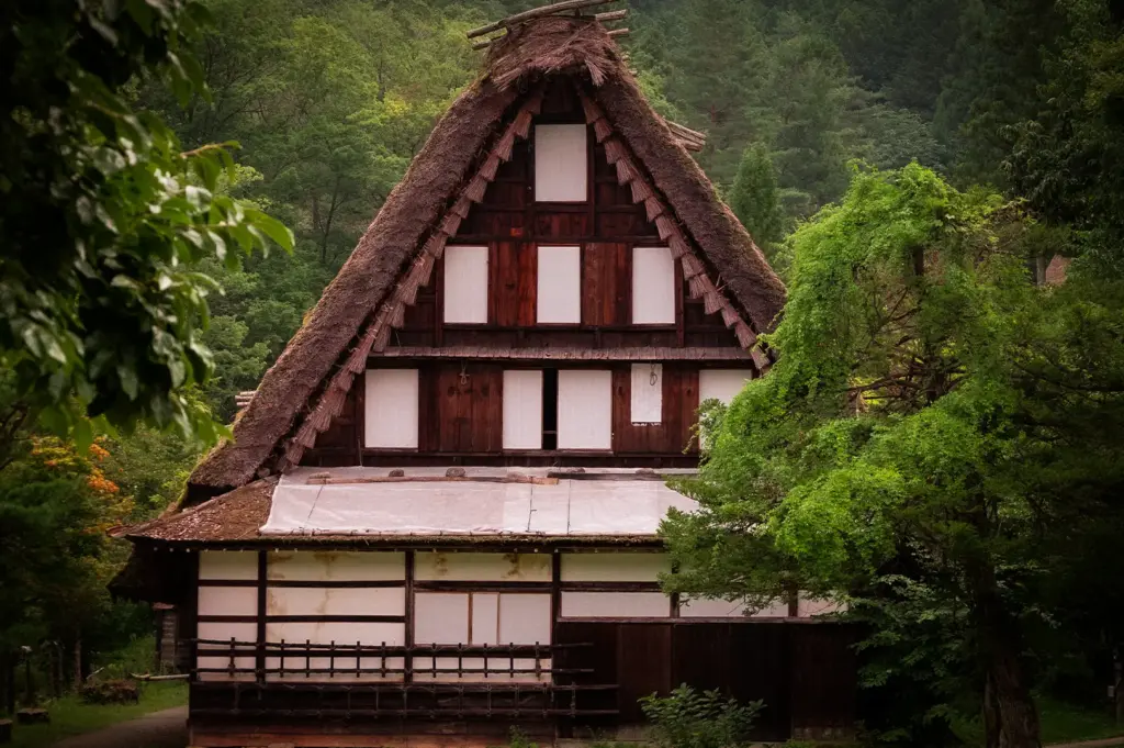 Traditional gassho-zukuri farmhouse surrounded by lush greenery near Takayama, Japan, featuring a steep thatched roof and classic Japanese alpine architecture.