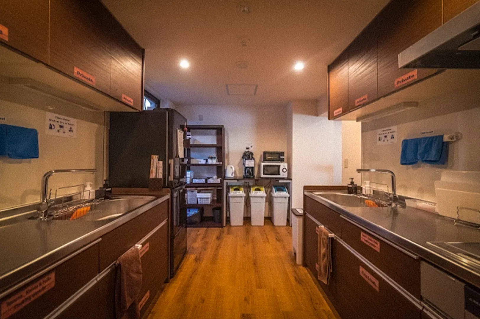 Spacious communal kitchen at K's House Kanazawa hostel featuring stainless steel worktops, multiple sinks, cooking facilities, storage shelves, microwave, refrigerator, and recycling stations for guest use.
