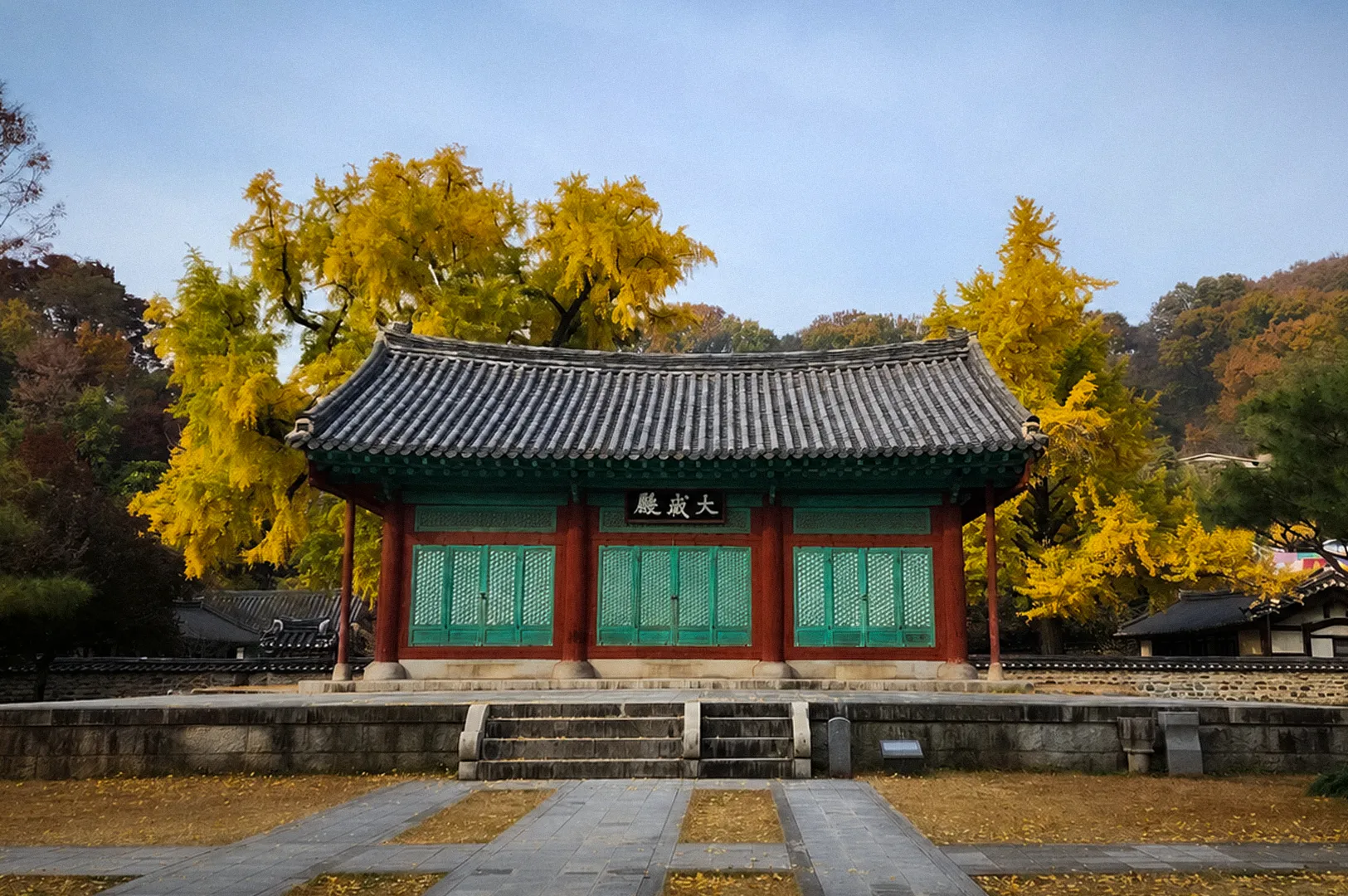 Daeseongjeon Hall at Jeonju Hyanggyo in Jeonju, South Korea, surrounded by golden ginkgo trees and autumn foliage, with a traditional Korean tiled roof and stone courtyard in front.