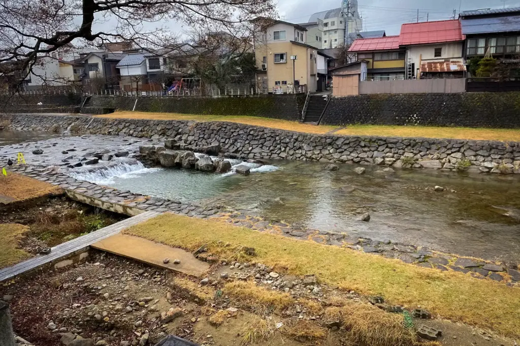 Miyagawa Morning Market riverside in Takayama, Japan, featuring the scenic Miyagawa River, stone embankments, and traditional neighborhood surrounding the popular market area.