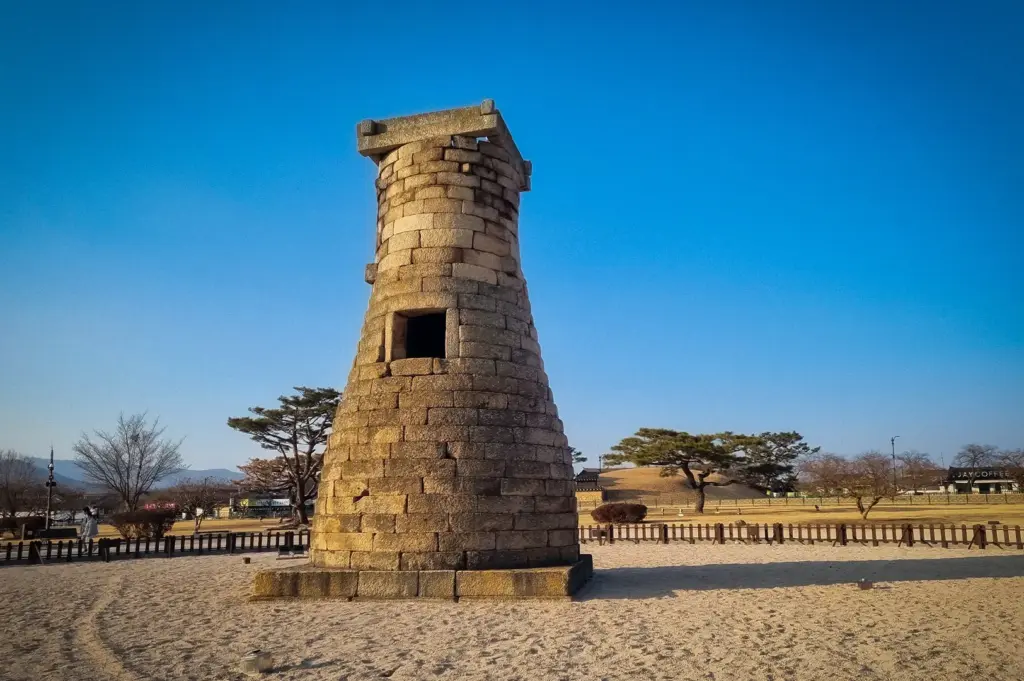 Cheomseongdae Observatory in Gyeongju, South Korea, featuring the ancient stone astronomical tower standing in an open historic park under a clear blue sky.