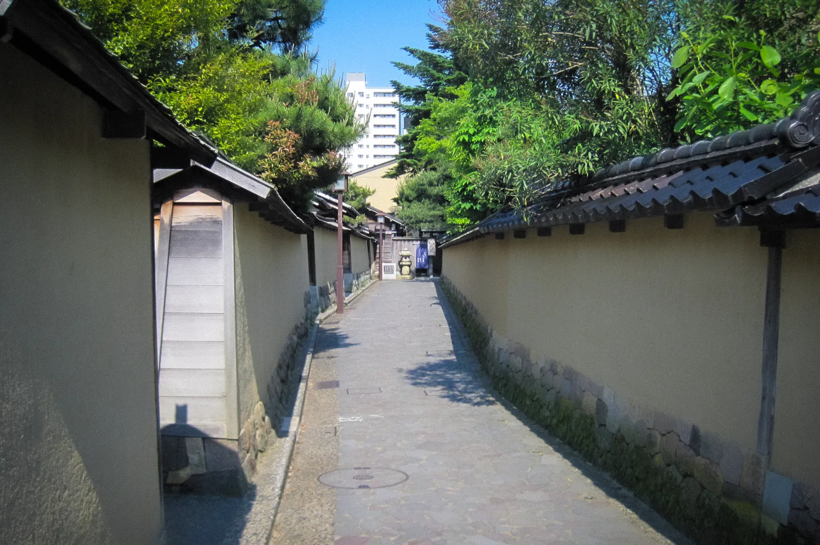 Stone-paved lane in Nagamachi Samurai District, Kanazawa, Japan, lined with traditional earthen walls, historic residences, and lush greenery.