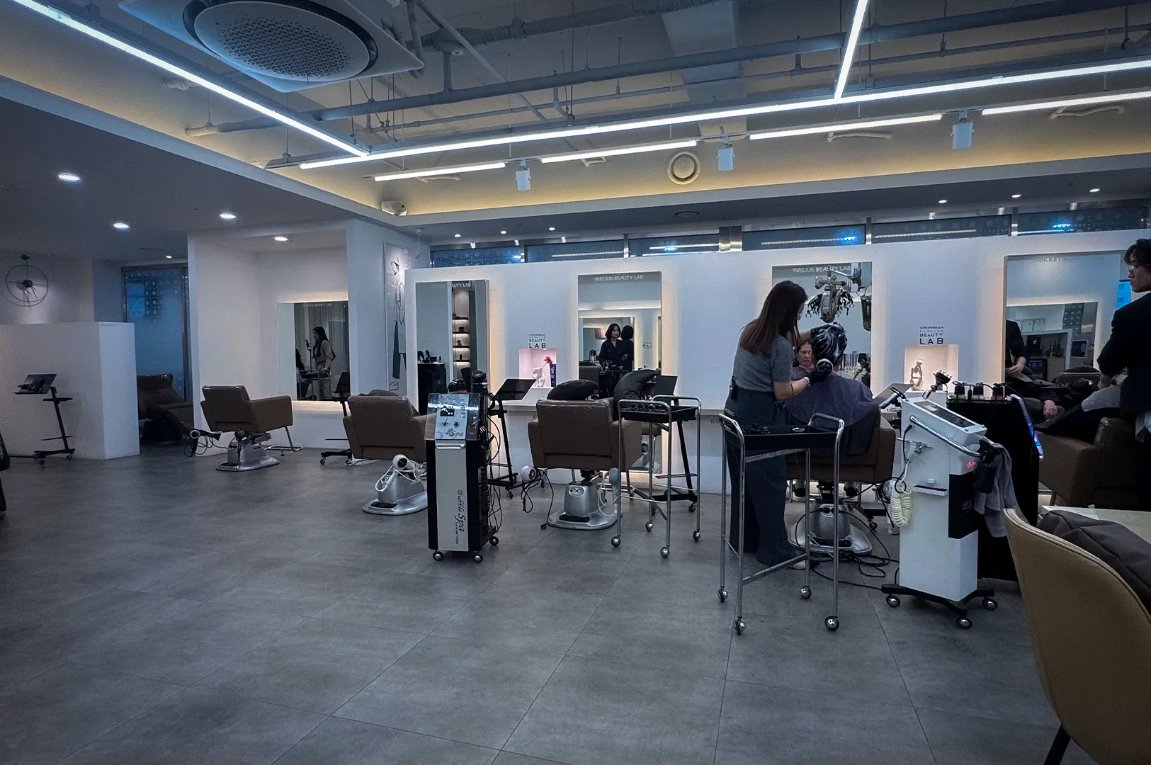Interior of Parkjun Beauty Lab, a modern Korean hair salon featuring professional styling stations, salon chairs, hair treatment equipment, and stylists providing beauty and haircare services in a spacious contemporary setting.