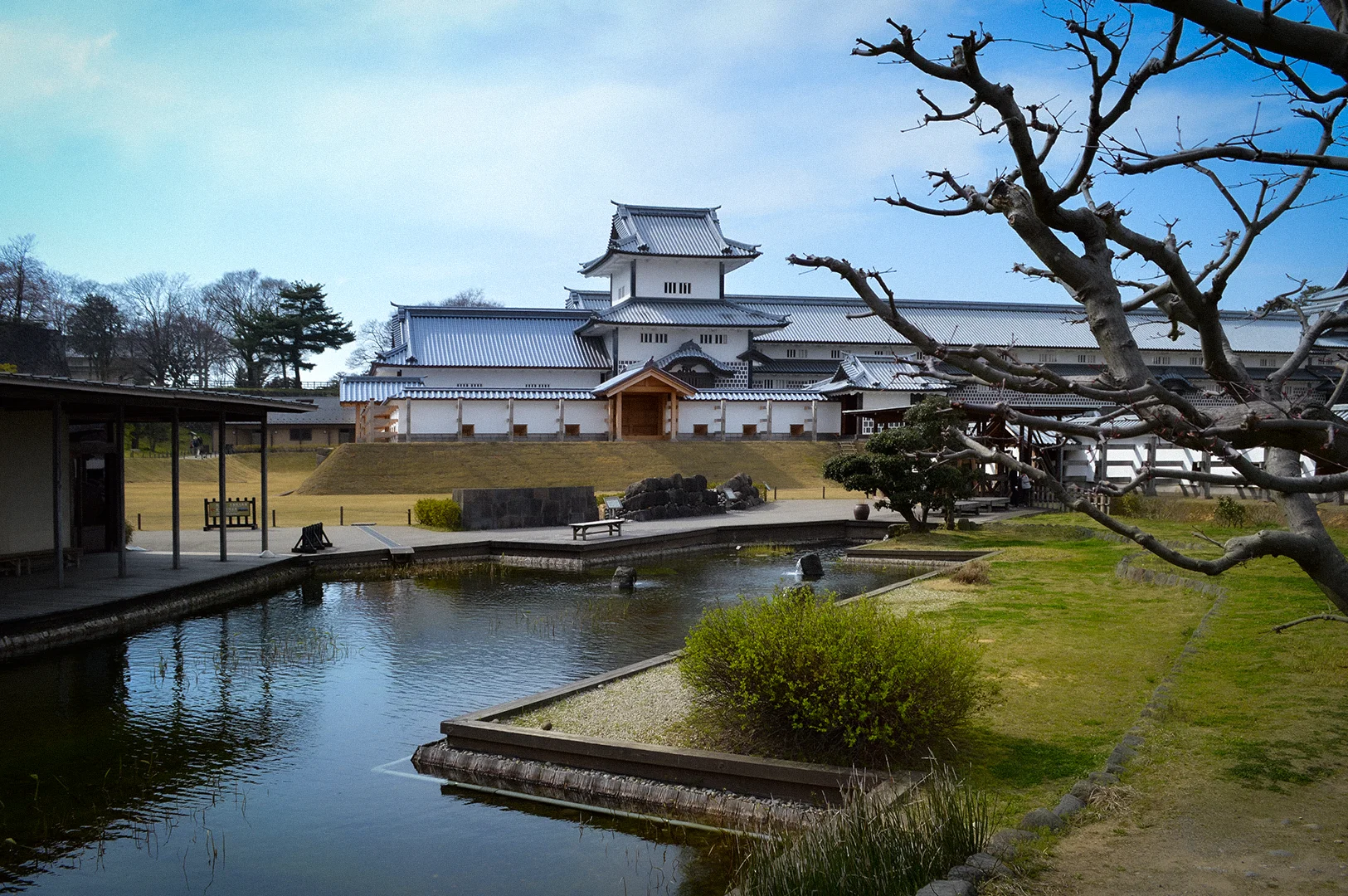 Kanazawa Castle viewed across Tsurunomaru Pond in Kanazawa, Japan, featuring traditional white castle architecture, landscaped gardens, calm water reflections, and scenic grounds.