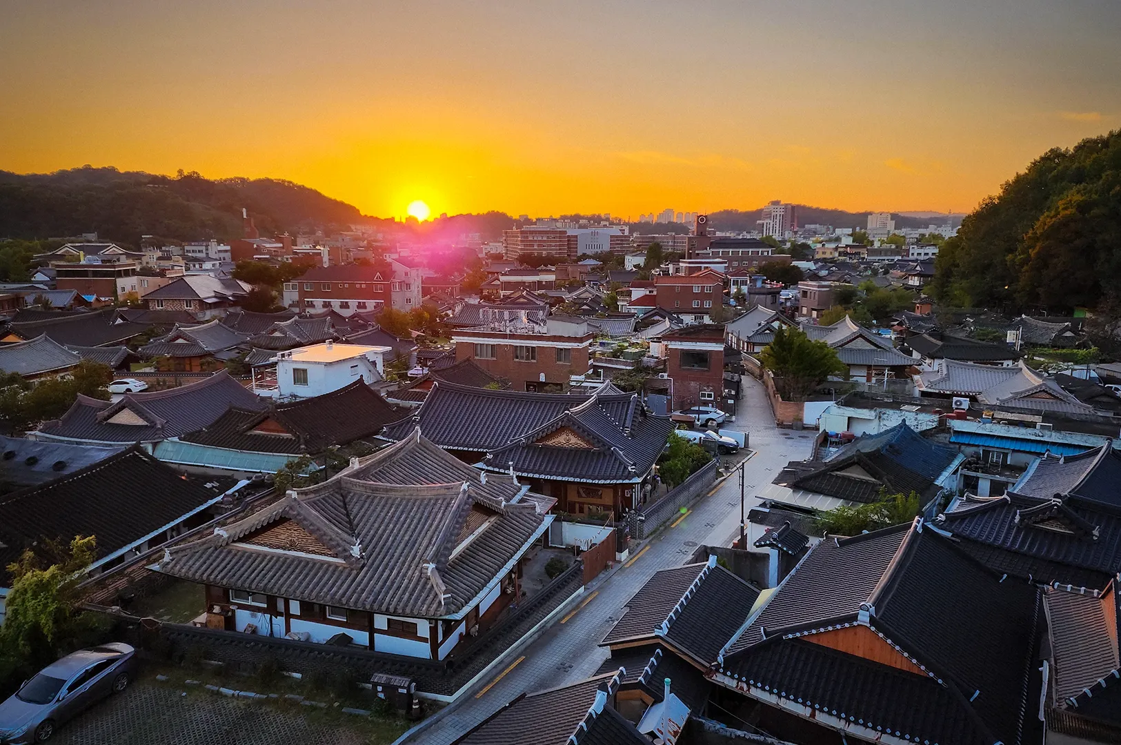 Sunset view over Jaman Mural Village in Jeonju, South Korea featuring traditional hanok rooftops, hillside scenery and warm golden light across the cityscape.