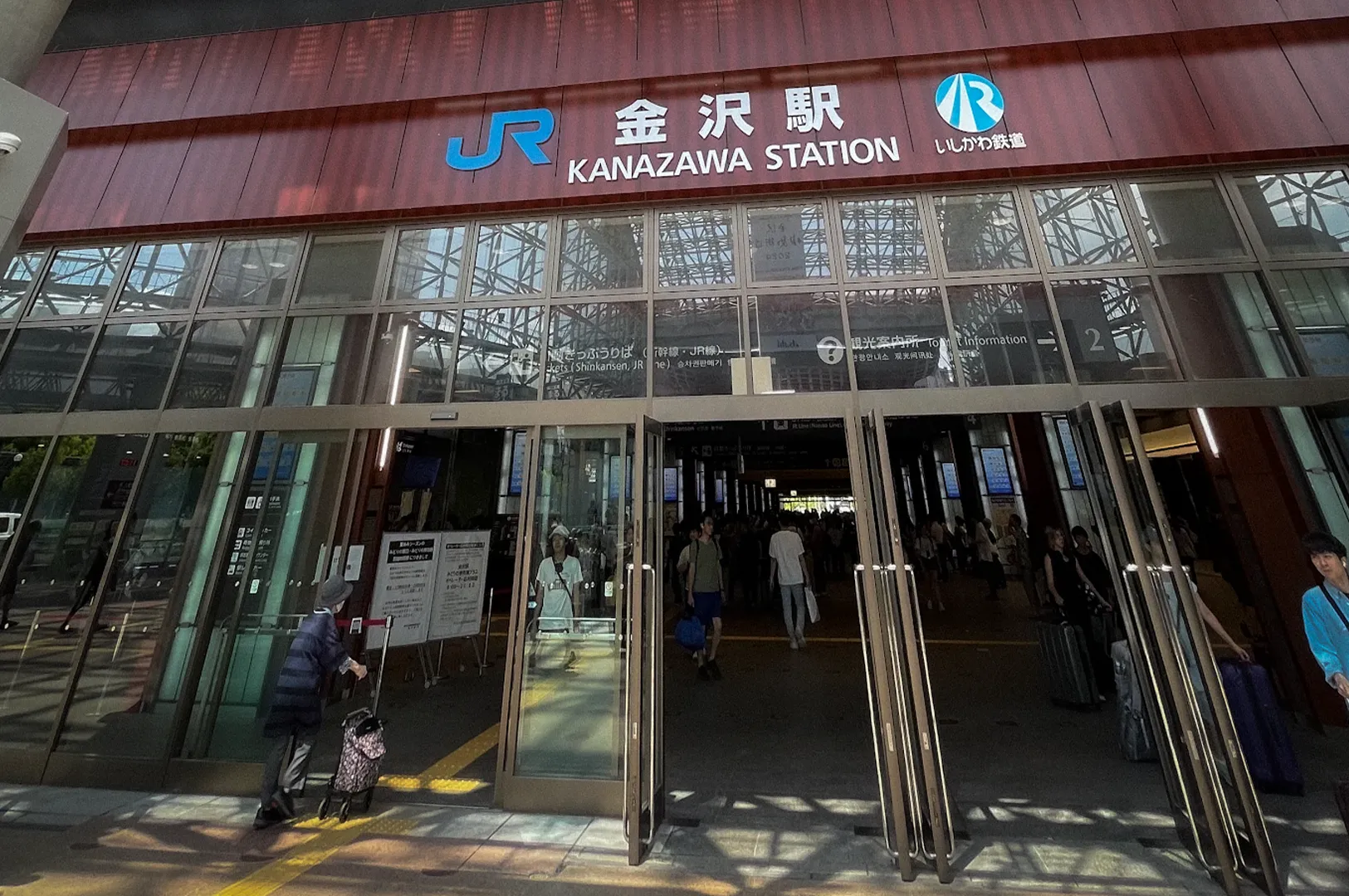 Main entrance of Kanazawa Station in Ishikawa Prefecture, Japan, featuring the modern steel-and-glass Motenashi Dome structure above the JR Kanazawa Station entrance with travelers entering and exiting the terminal.