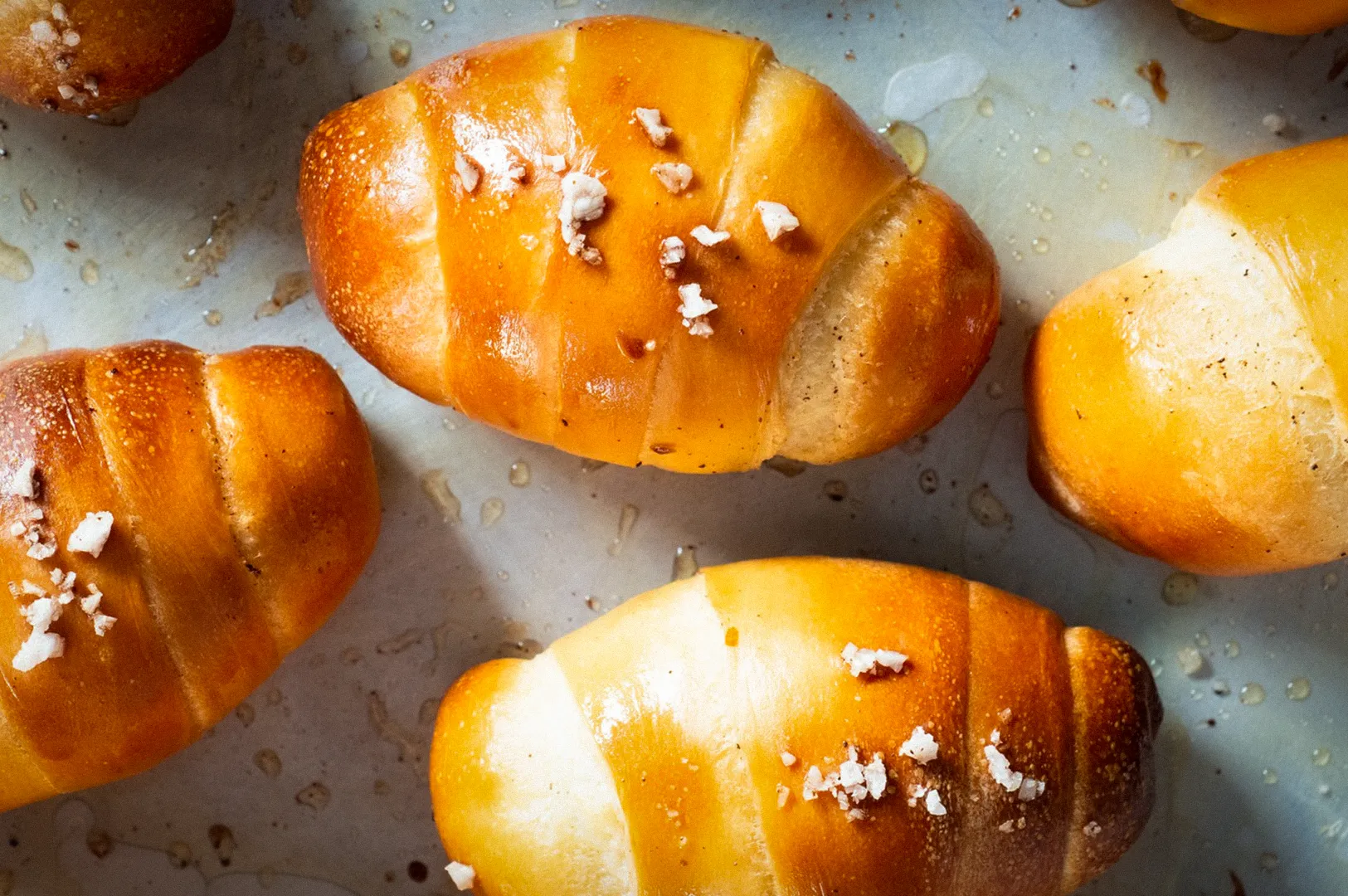 Freshly baked Korean salt bread rolls with a golden-brown crust, topped with coarse sea salt crystals and butter glaze, arranged on a baking tray. A popular Korean bakery pastry known for its soft interior and savory buttery flavor.