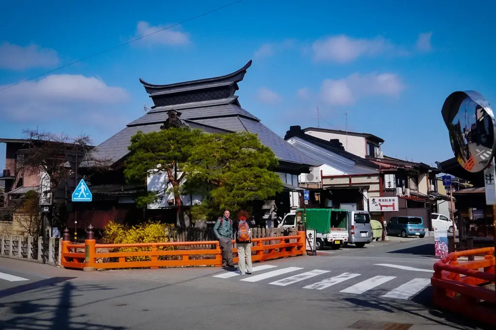 Traditional streetscape in Takayama Old Town, Japan, featuring historic wooden buildings, a red bridge railing, and preserved Edo-period architecture under a clear blue sky.