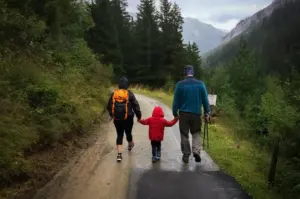 Family hiking along a scenic forest trail surrounded by mountains and evergreen trees, enjoying an outdoor nature adventure on a misty day.