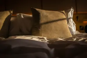 Comfortable hotel bed with plush pillows and crisp white linens illuminated by warm natural sunlight, creating a cozy and inviting bedroom atmosphere.