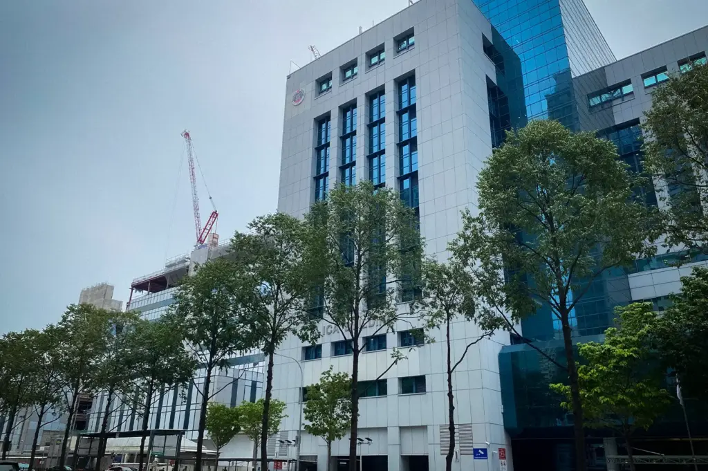 Immigration & Checkpoints Authority (ICA) building in Singapore viewed from the street with modern architecture, roadside trees, and a clear daytime sky.