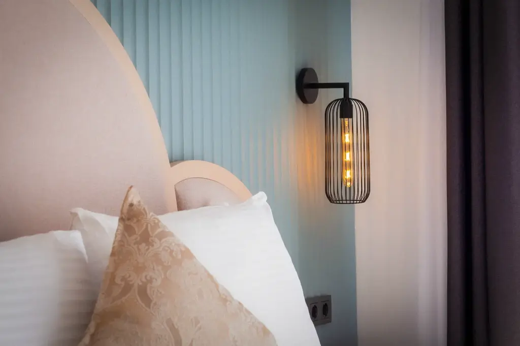 Close-up of a luxury hotel bedroom featuring plush pillows, an upholstered headboard, modern wall lighting, and elegant contemporary interior design.
