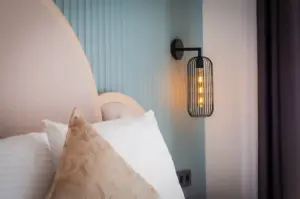 Close-up of a luxury hotel bedroom featuring plush pillows, an upholstered headboard, modern wall lighting, and elegant contemporary interior design.