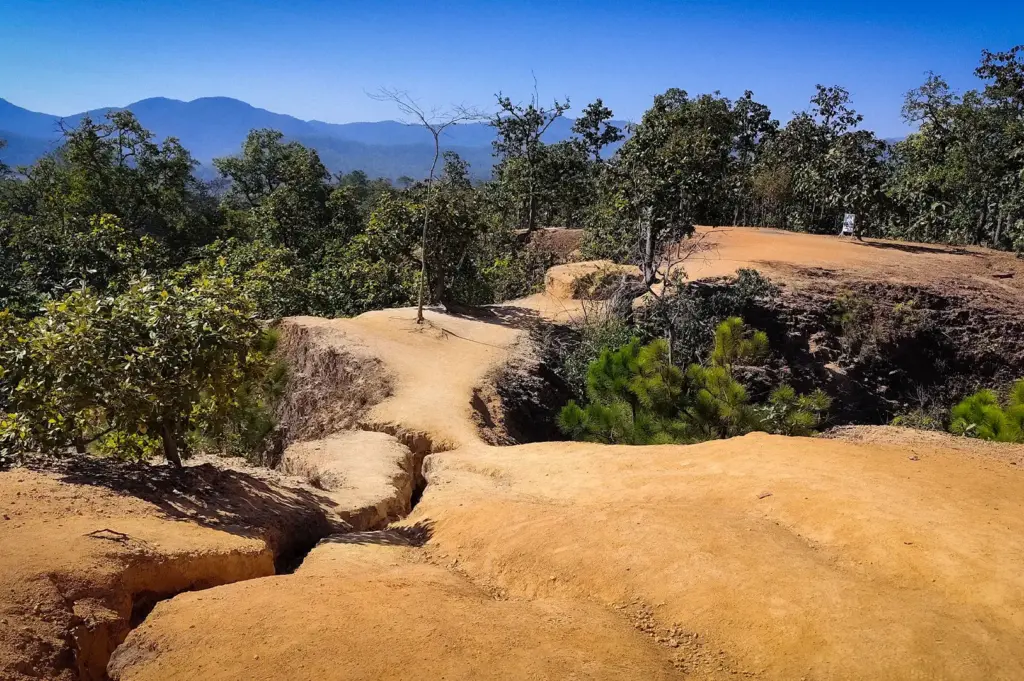 Scenic hiking trail at Pai Canyon in Thailand with rugged sandstone ridges, lush forest, and mountain views under a clear blue sky.