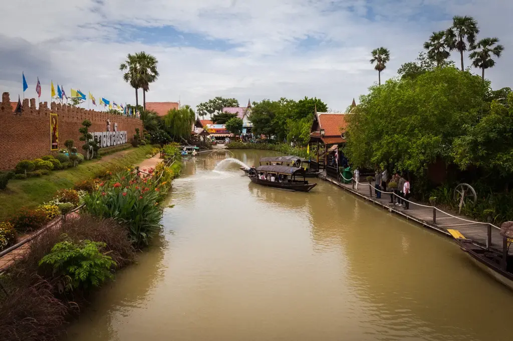 Scenic canal in Ayutthaya, Thailand featuring traditional Thai architecture, wooden boats, lush gardens, and waterfront walkways near the historic city.
