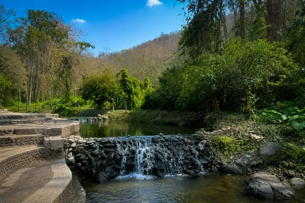 Natural hot springs in Pai, Thailand featuring cascading pools, lush tropical forest, stone walkways, and a peaceful outdoor setting.