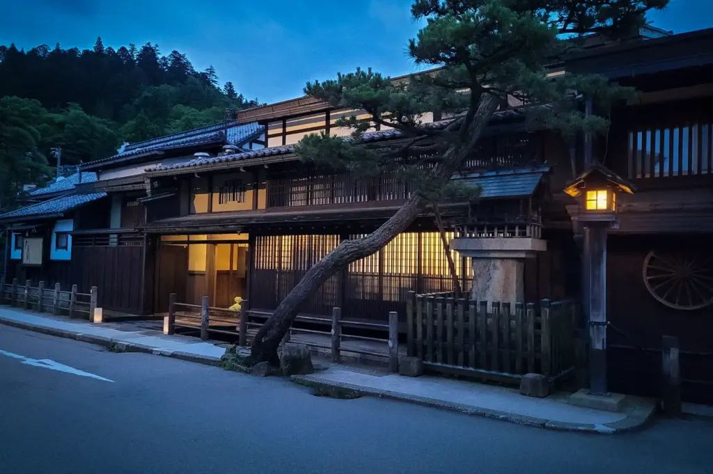 Traditional wooden merchant houses along Sanmachi Suji in Takayama, Japan, illuminated at dusk with classic lanterns, preserved Edo-period architecture, and a peaceful historic streetscape.