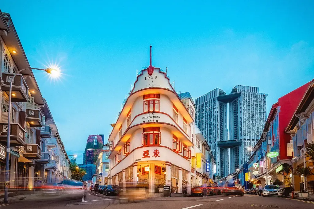 Historic shophouses along Keong Saik Road in Singapore at dusk, featuring the iconic Potato Head building surrounded by modern skyscrapers and vibrant city streets.