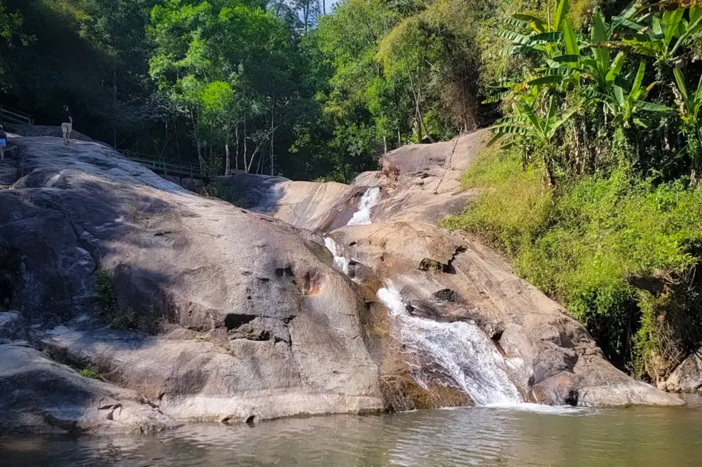 Mor Paeng Waterfall in Pai, Thailand featuring cascading water over smooth rock formations surrounded by lush tropical forest and a natural swimming pool.