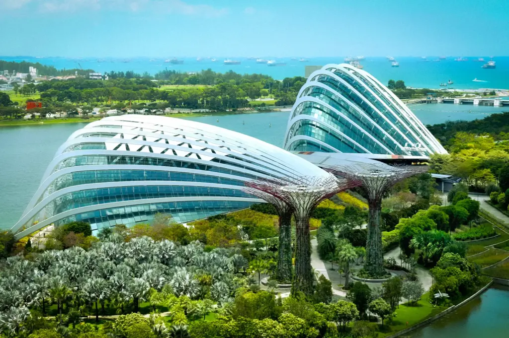 Aerial view of Gardens by the Bay in Singapore featuring the Supertree Grove, Flower Dome, Cloud Forest conservatories, and the Marina Bay waterfront on a sunny day.