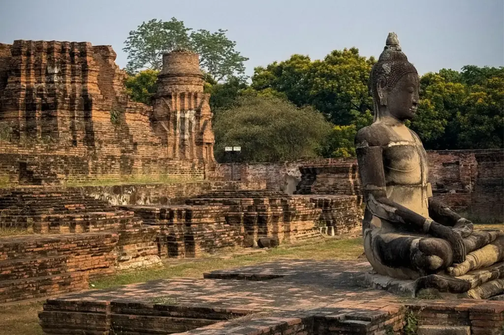 Ancient seated Buddha statue surrounded by the historic brick ruins of Wat Mahathat in Ayutthaya Historical Park, Thailand.