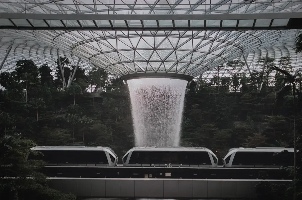 Jewel Changi Airport Rain Vortex in Singapore with the indoor waterfall cascading beneath the glass dome and Skytrain passing through the lush forest.