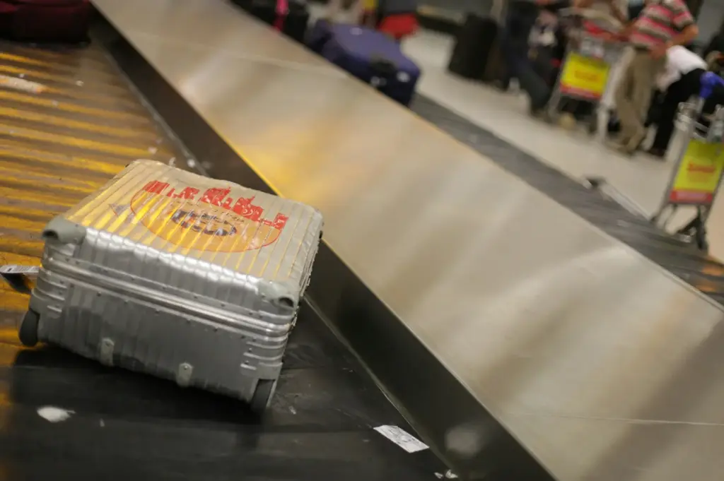 Suitcase on an airport baggage claim carousel in Singapore with travelers waiting to collect their luggage at the arrivals hall.