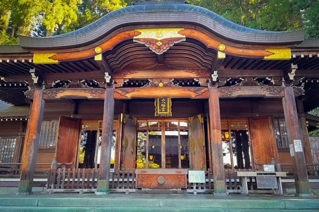 Front view of Sakurayama Hachimangu Shrine in Takayama, Japan, showcasing its ornate wooden architecture, curved roof, intricate carvings, and historic Shinto shrine entrance surrounded by trees.