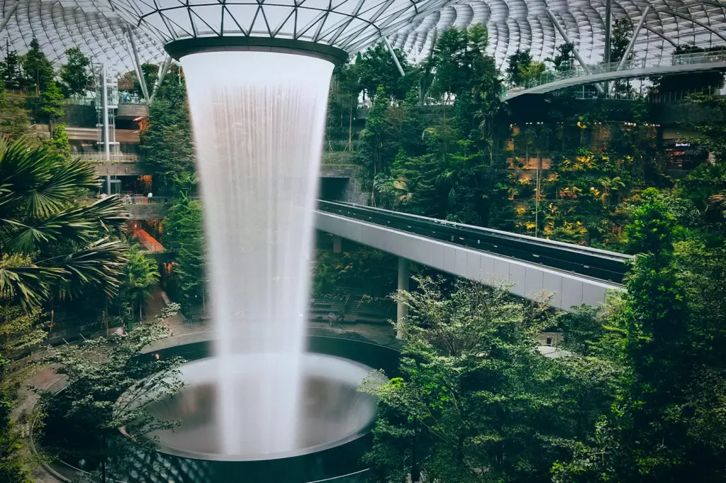 The HSBC Rain Vortex inside Jewel Changi Airport in Singapore, surrounded by lush indoor gardens, walking trails, and the iconic glass dome architecture.