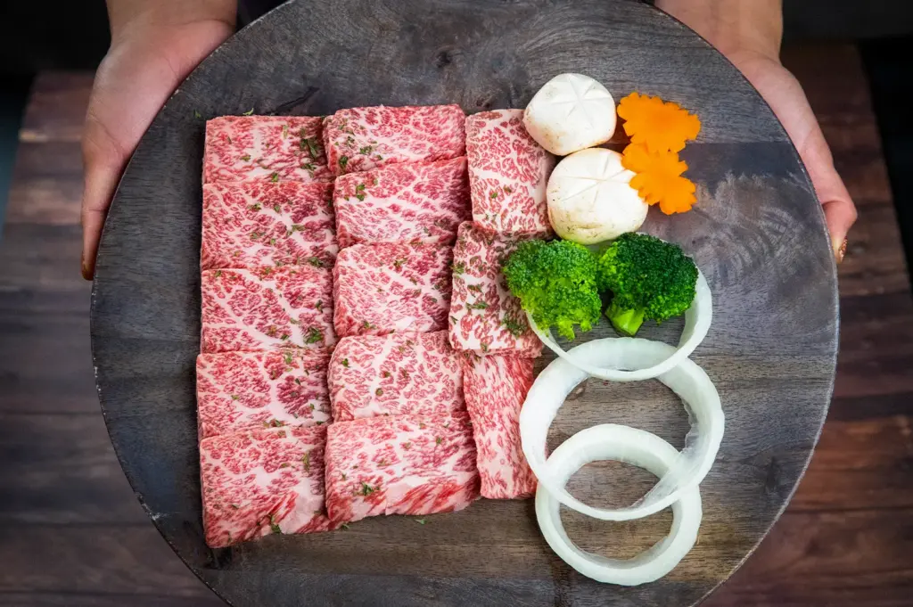 Beautifully marbled Japanese A5 Wagyu beef slices arranged on a wooden serving platter with mushrooms, broccoli, onion rings, and carved carrots, ready for yakiniku or shabu-shabu dining.