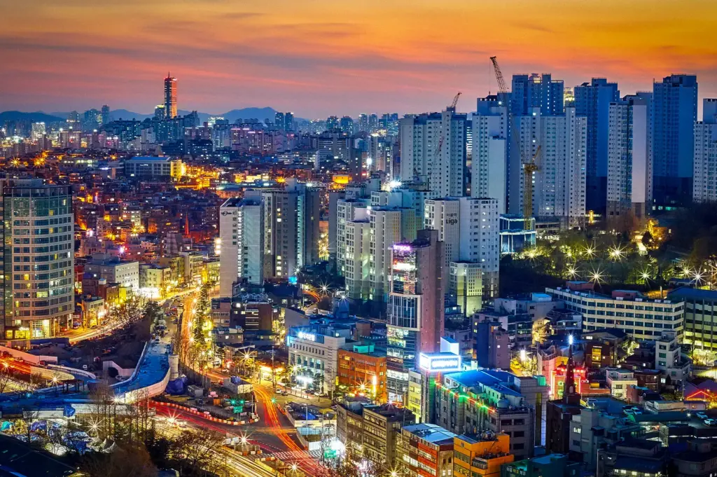 Panoramic view of Seoul, South Korea at sunset featuring a vibrant city skyline, illuminated skyscrapers, busy streets, and modern urban architecture.
