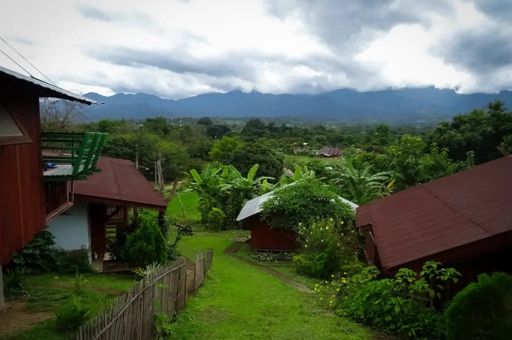 Scenic mountain village in Pai, Thailand featuring traditional wooden houses, lush greenery, and panoramic views of the surrounding mountains.